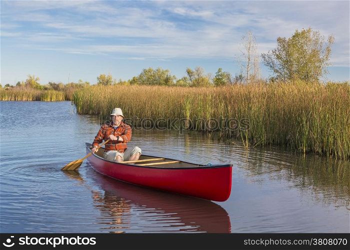 senior male paddler paddling a red canoe on a calm lake, Riverbend Ponds Natural Area, Fort Collins, Colorado