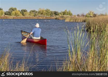 senior male paddler paddling a red canoe on a calm lake, Riverbend Ponds Natural Area, Fort Collins, Colorado