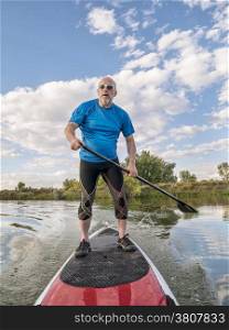 senior male paddler paddling a stand up paddleboard (SUP), calm lake in Colorado, late summer