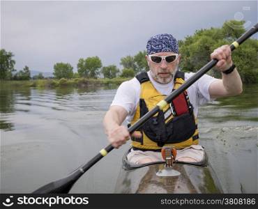 senior male paddler training in a narrow fast racing kayak on a lake, focus on paddler&rsquo;s face