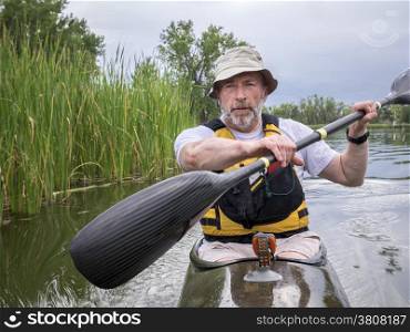 senior male paddler training in a narrow fast racing kayak on a lake in Colorado