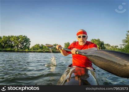 senior male paddler training in a racing sea kayak with a wing paddle on a lake, motion blur of paddle