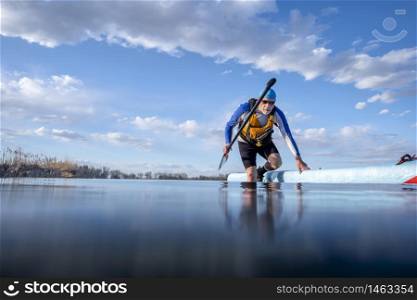 senior male paddler with his stand up paddleboard on a shore of calm lake, low angle view form action camera, recreation, fitness and training concept