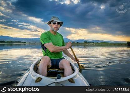 senior male paddling an expedition canoe on lake at dusk with Front Range of Rocky Mountains in background
