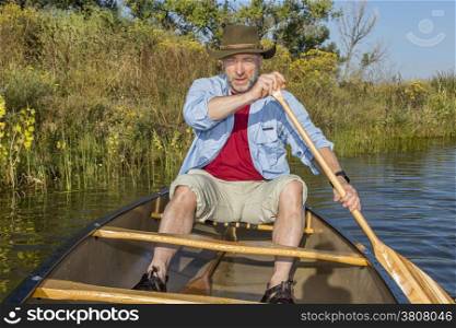 senior male paddling canoe on lake in late summer, Fort Collins, Colorado