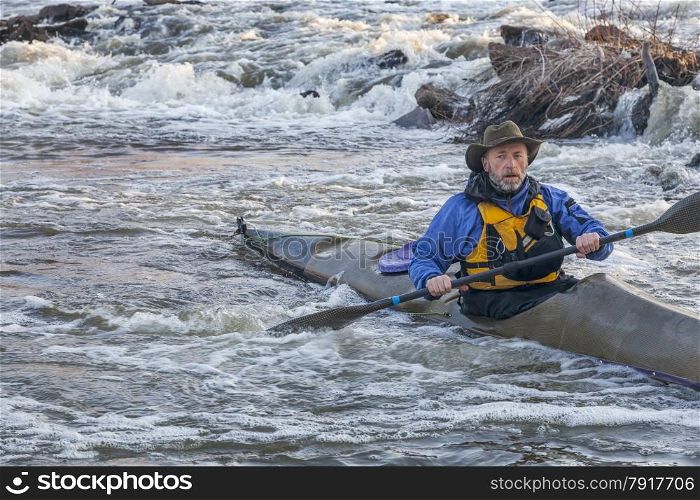 senior male paddling sea kayak through river rapids