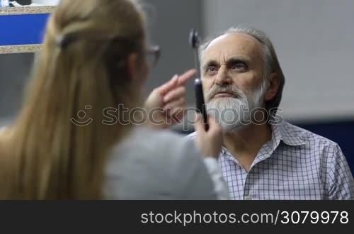 Senior male patient with beard checking nervous system by professional neurologist in medical office. Elderly man folowing test hammer during medical exam in hospital. Female neurologist testing reflexes of patient&acute;s eyes using test hammer.