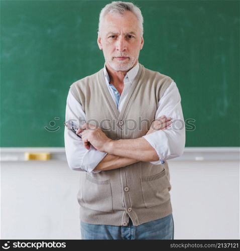 senior male professor with arms crossed standing against chalkboard