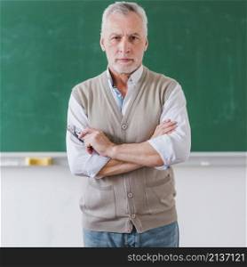 senior male professor with arms crossed standing against chalkboard