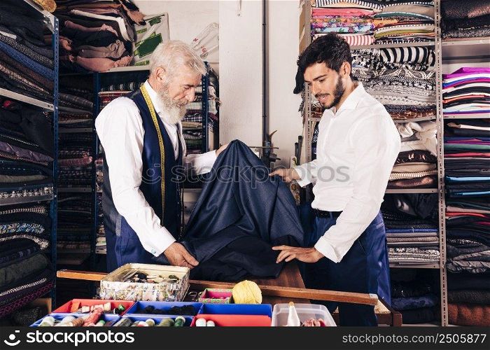 senior male seller offering fabrics young man textile shop