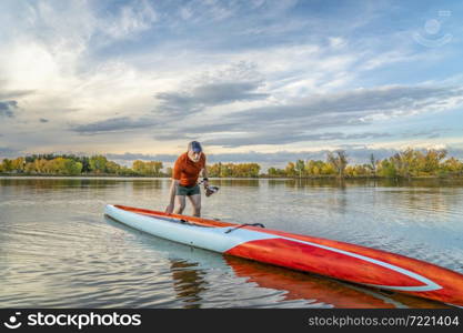 senior male stand up paddler is launching his long racing paddleboard on a lake in Colorado, fall scenery