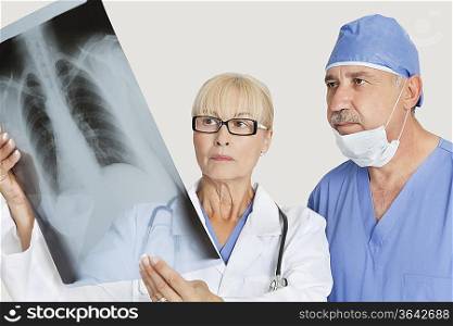 Senior male surgeon and female doctor looking at x-ray over gray background