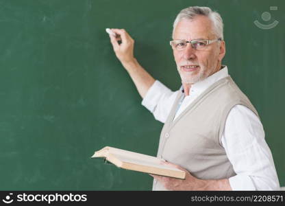 senior male teacher holding book writing blackboard