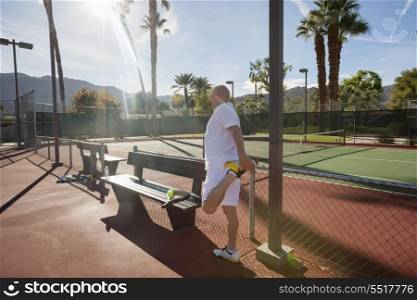 Senior male tennis player stretching leg on court