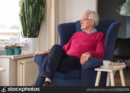 Senior man alone sitting in chair and looking outside