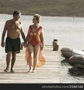Senior man and a mature woman holding each other&acute;s hands and walking on a jetty