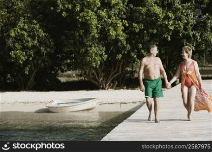 Senior man and a mature woman holding each other&acute;s hands and walking on a jetty