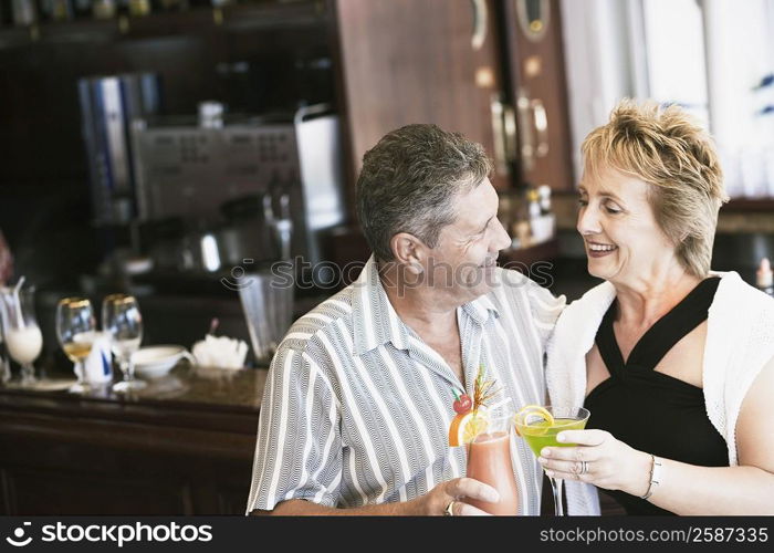 Senior man and a mature woman holding glasses of cocktail and standing at a bar counter