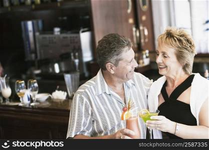Senior man and a mature woman holding glasses of cocktail and standing at a bar counter
