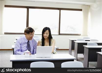 Senior man and a young woman using a laptop in a classroom