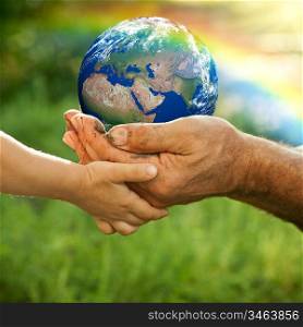 Senior man and baby holding the Earth in hands against a rainbow in spring. Ecology concept