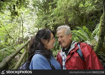 Senior man and middle-aged woman in forest, looking in eyes, smiling