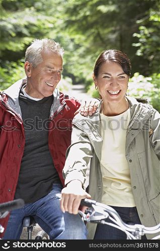 Senior man and middle-aged woman on bikes in forest, laughing