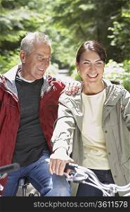 Senior man and middle-aged woman on bikes in forest, laughing