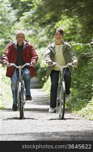 Senior man and middle-aged woman riding bicycles in forest, front view