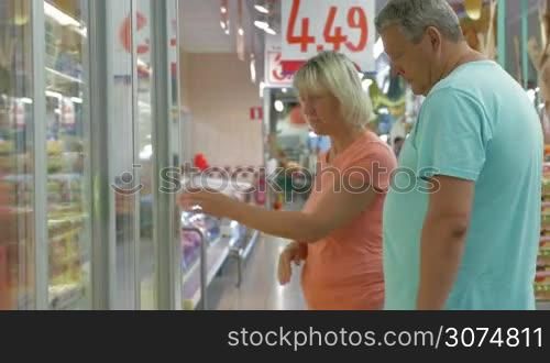 Senior man and woman choosing butter at the fridge section of supermarket, they taking some packages and checking them