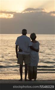 Senior man and woman couple embracing at sunset or sunrise on a deserted tropical beach