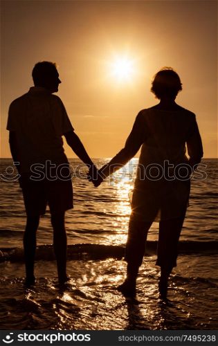 Senior man and woman couple holding hands at sunset or sunrise on a deserted tropical beach