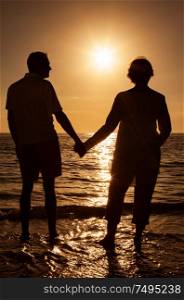 Senior man and woman couple holding hands at sunset or sunrise on a deserted tropical beach