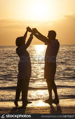 Senior man and woman couple holding hands dancing at sunset or sunrise on a deserted tropical beach