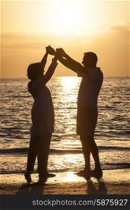 Senior man and woman couple holding hands dancing at sunset or sunrise on a deserted tropical beach