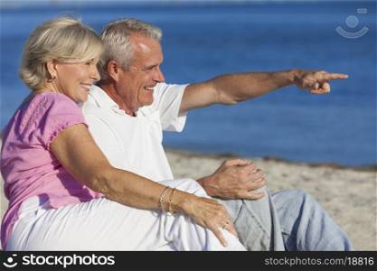 Senior man and woman couple sitting on a deserted beach pointing to the sea