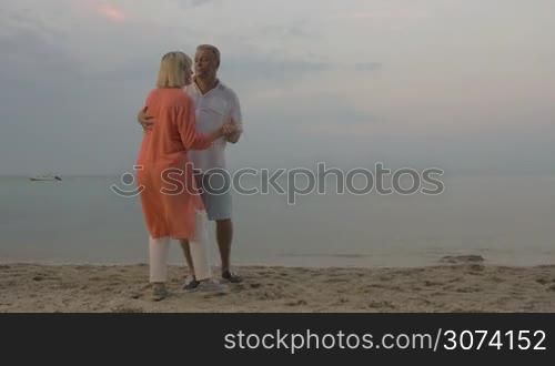 Senior man and woman having romantic evening on the shore. Happy couple enjoying slow dance by the sea