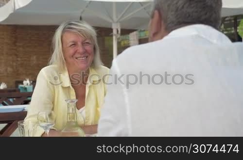Senior man and woman sitting in street cafe on summer day. They have lively talk as woman is rather cheerful and excited