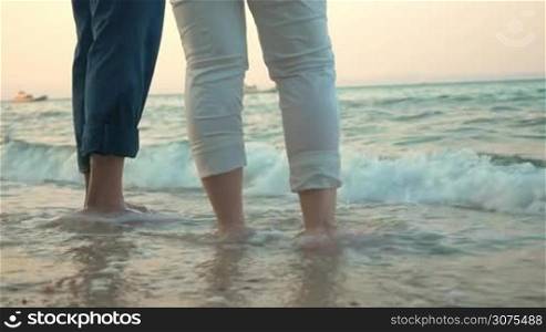 Senior man and woman standing on the beach and sea waves washing their feet