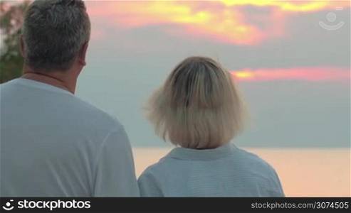 Senior man and woman turning, embracing and smiling to the camera. Sunset and sea in background. Copy space on the right