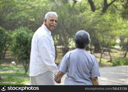 Senior man and woman walking in park while holding hands