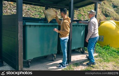 Senior man and young man throwing garbage to container. Men throwing garbage to container