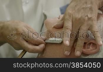 Senior man at work as barber shaving customer with razor in old fashion shop or men&acute;s beauty parlor