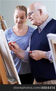 Senior Man Attending Painting Class With Teacher