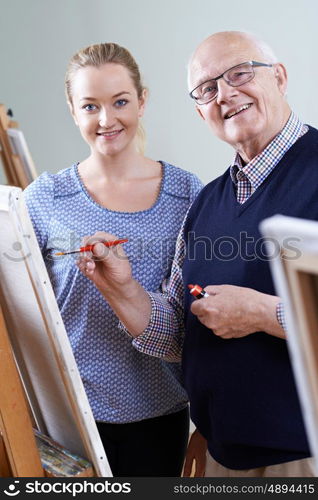 Senior Man Attending Painting Class With Teacher