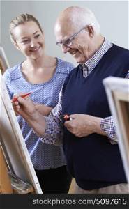 Senior Man Attending Painting Class With Teacher