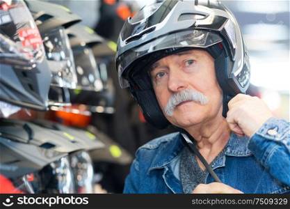 senior man choosing a trendy motorcycles helmet in a shop