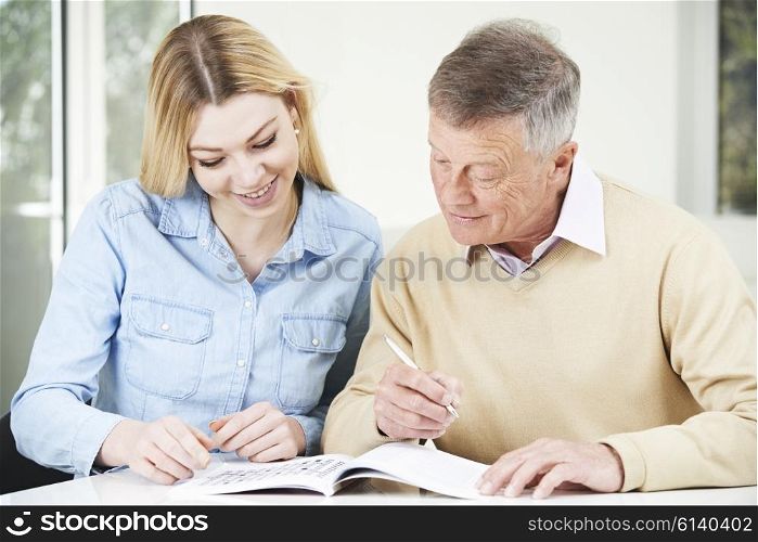 Senior Man Completing Crossword Puzzle With Teenage Granddaughter Daughter