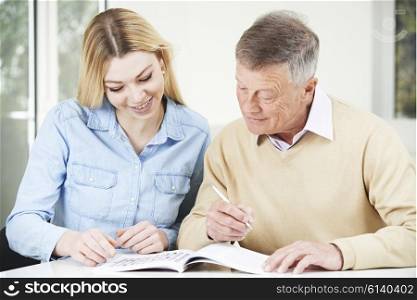 Senior Man Completing Crossword Puzzle With Teenage Granddaughter Daughter