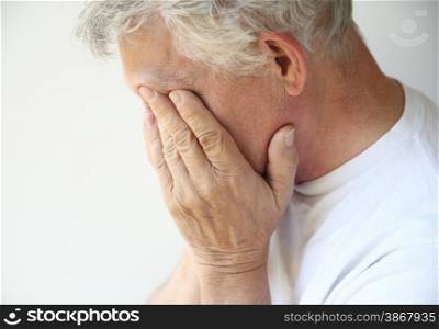 Senior man covers his face with his hands.